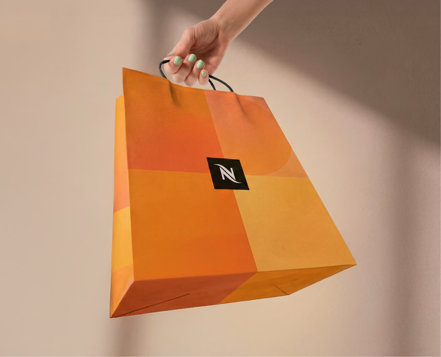 Hand holding an orange shopping bag with the Nespresso logo on a beige background.