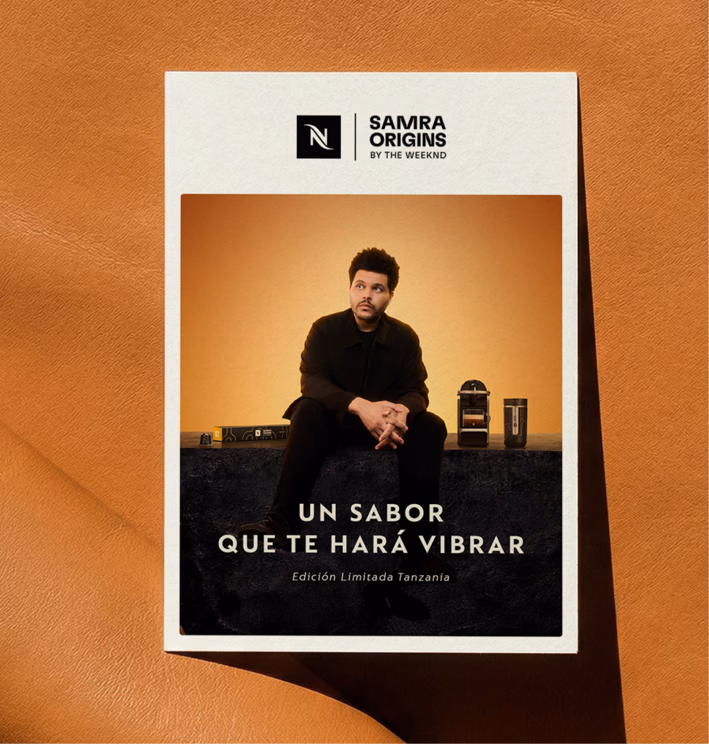Nespresso Samra Origins by The Weeknd coffee ad with man seated, coffee machine, and cup on orange background.