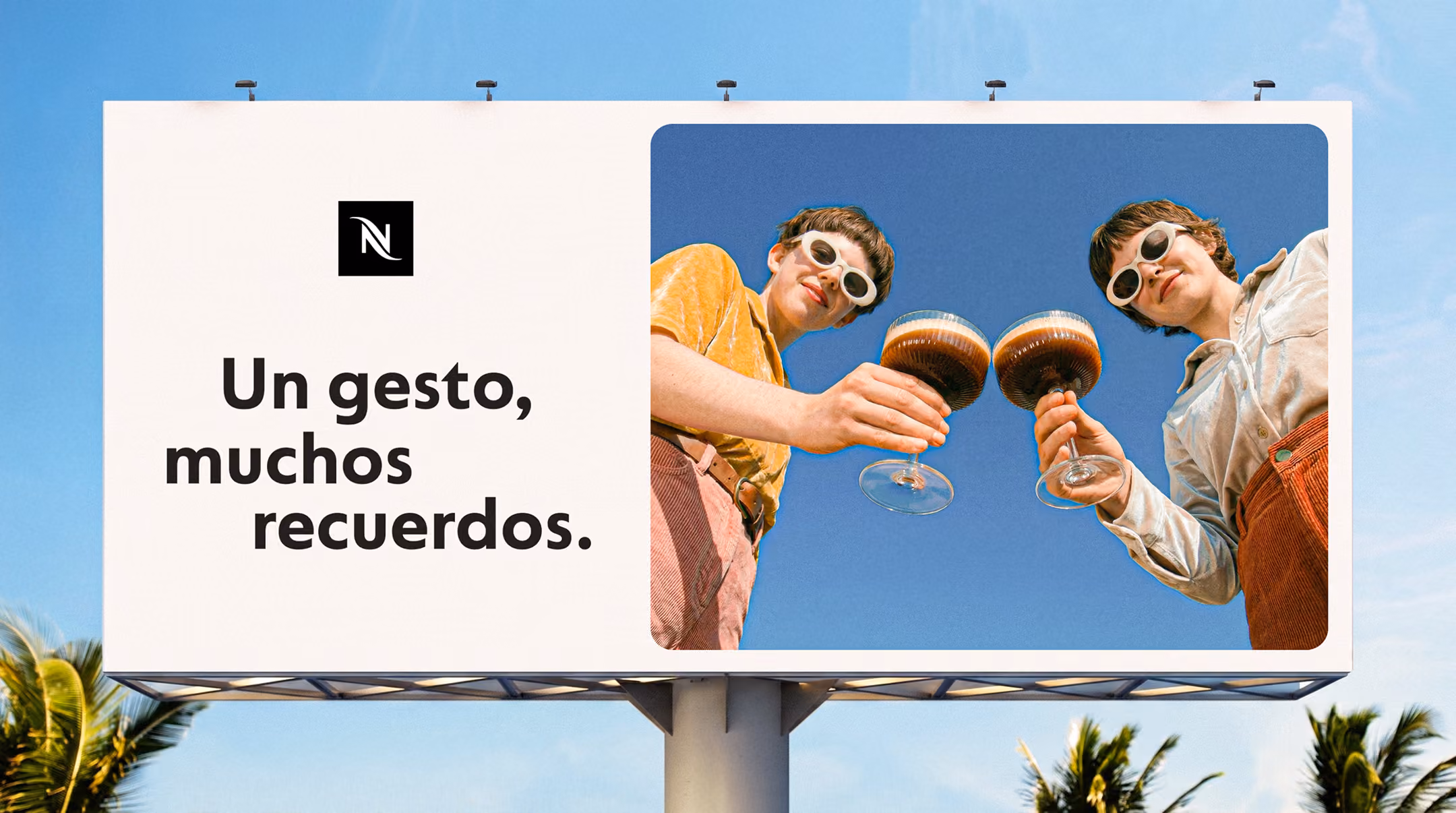 Billboard showing two people clinking coffee glasses under a clear blue sky, with Spanish text.
