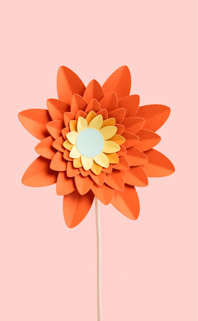 Orange and yellow layered paper flower with a light blue center on a thin white stem.