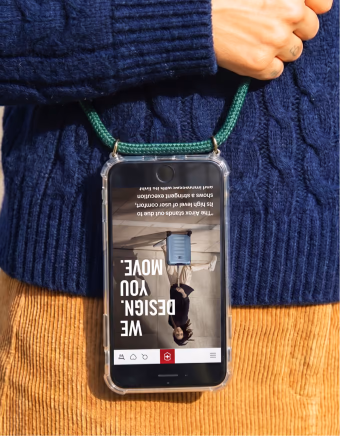 Person in blue sweater and brown pants holds phone with green lanyard displaying suitcase ad.
