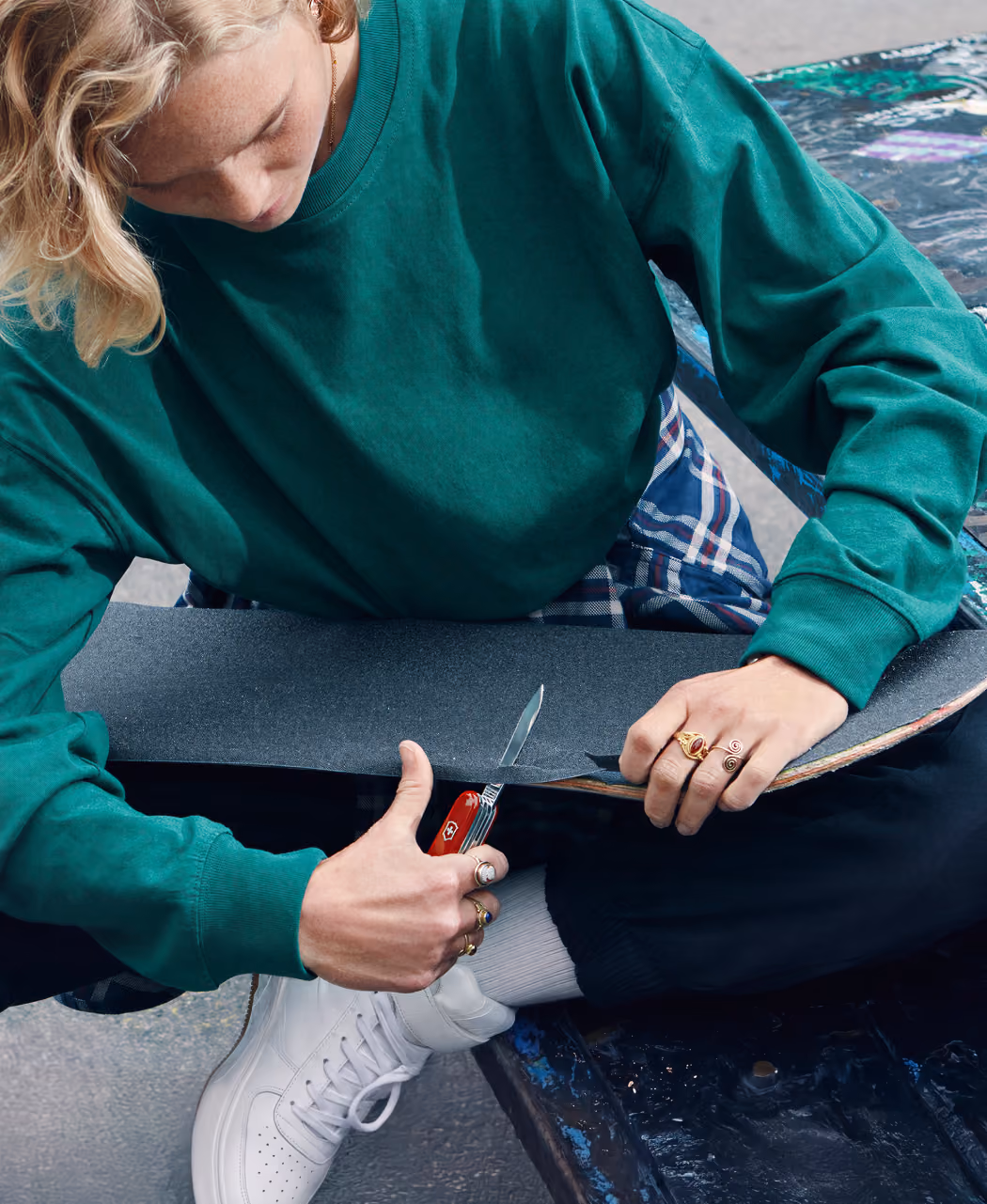 Person in green sweatshirt cuts skateboard grip tape using a red Swiss Army knife.