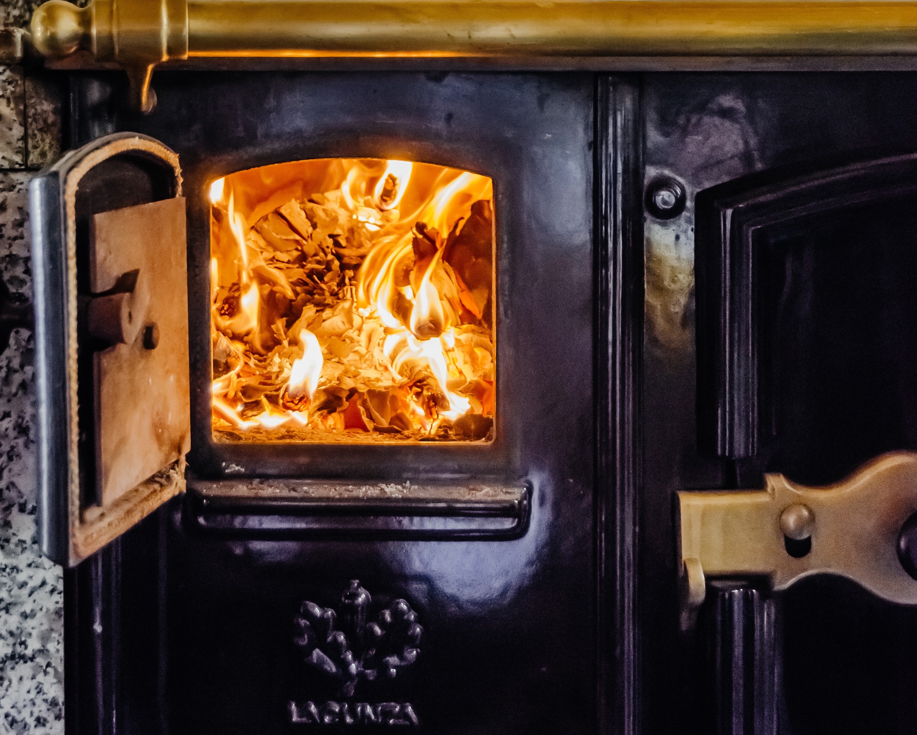 Close-up of an open black cast iron wood stove door with bright orange flames burning inside.