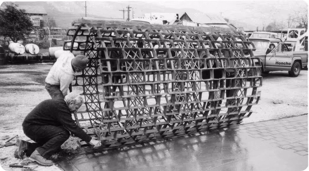 Two men assembling a large cylindrical metal grid structure outdoors next to a truck labeled 'Honcho'.