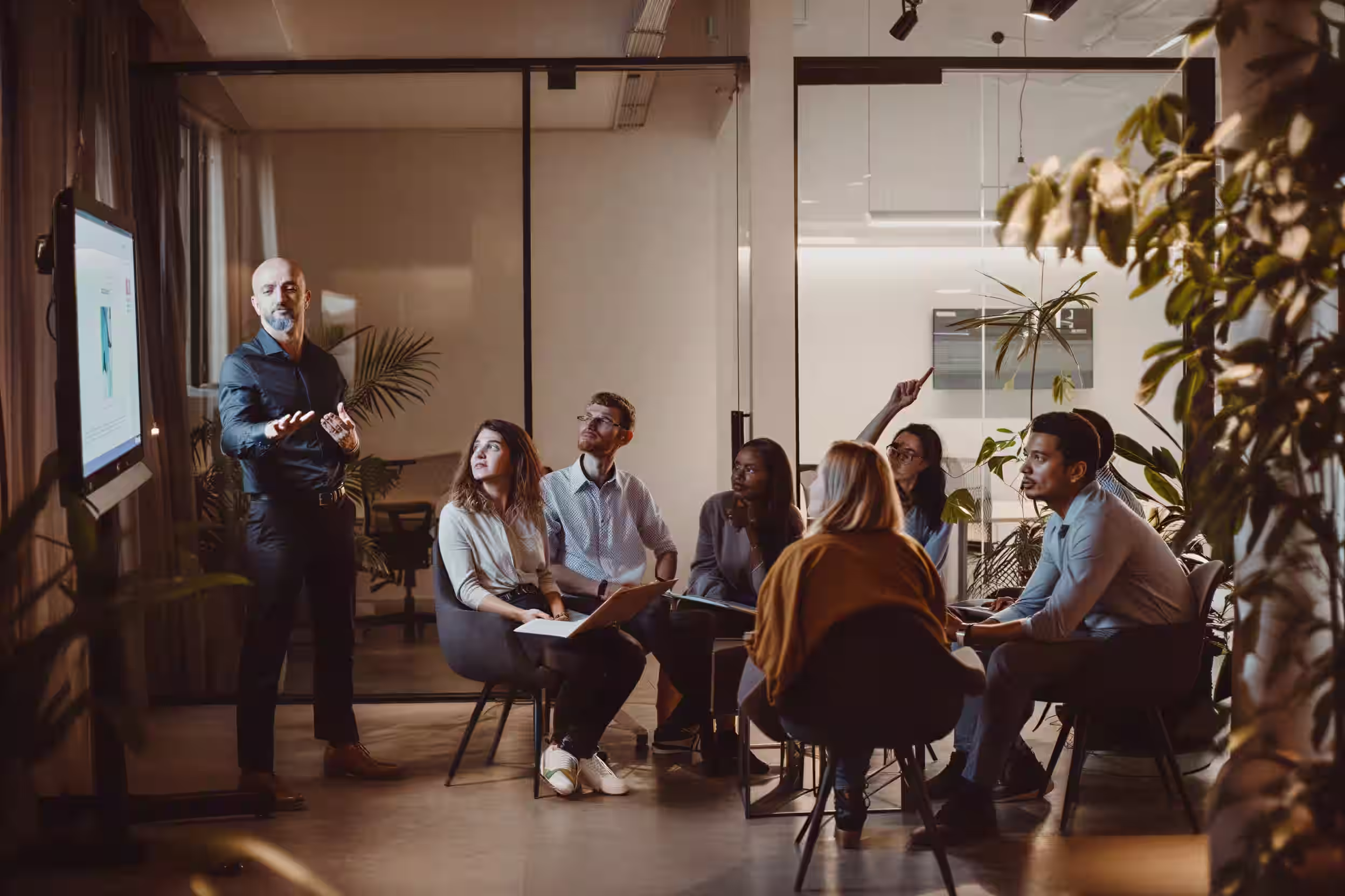 Fractional executive giving a presentation on cybersecurity to a diverse group of six seated colleagues in a modern office meeting room with glass walls and plants.