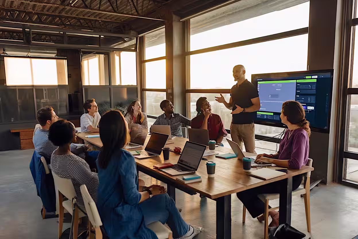 Cybersecurity meeting with diverse colleagues gathered around a table, with fractional executive standing and presenting using a large screen.