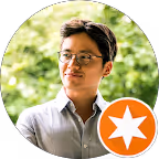 Junger Mann mit Brille und weißem Hemd vor unscharf grünem Hintergrund.