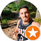 Mann mit dunklem Haar und Schnurrbart, der in einem Waldgebiet ein Selfie macht.