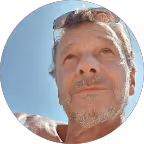 Nahaufnahme eines älteren Mannes mit grauem Bart unter blauem Himmel.