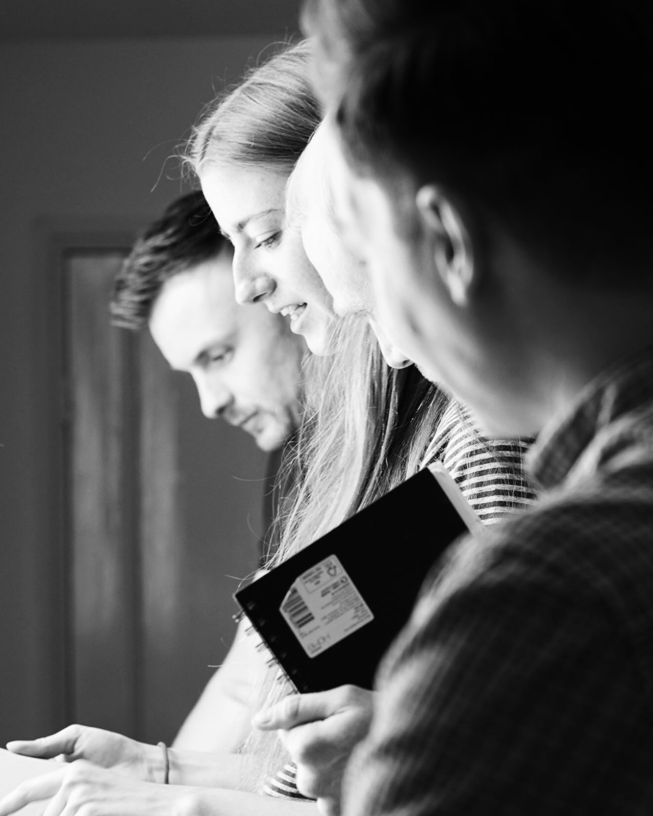 Four people closely gathered, looking down at something, one holding a notebook.