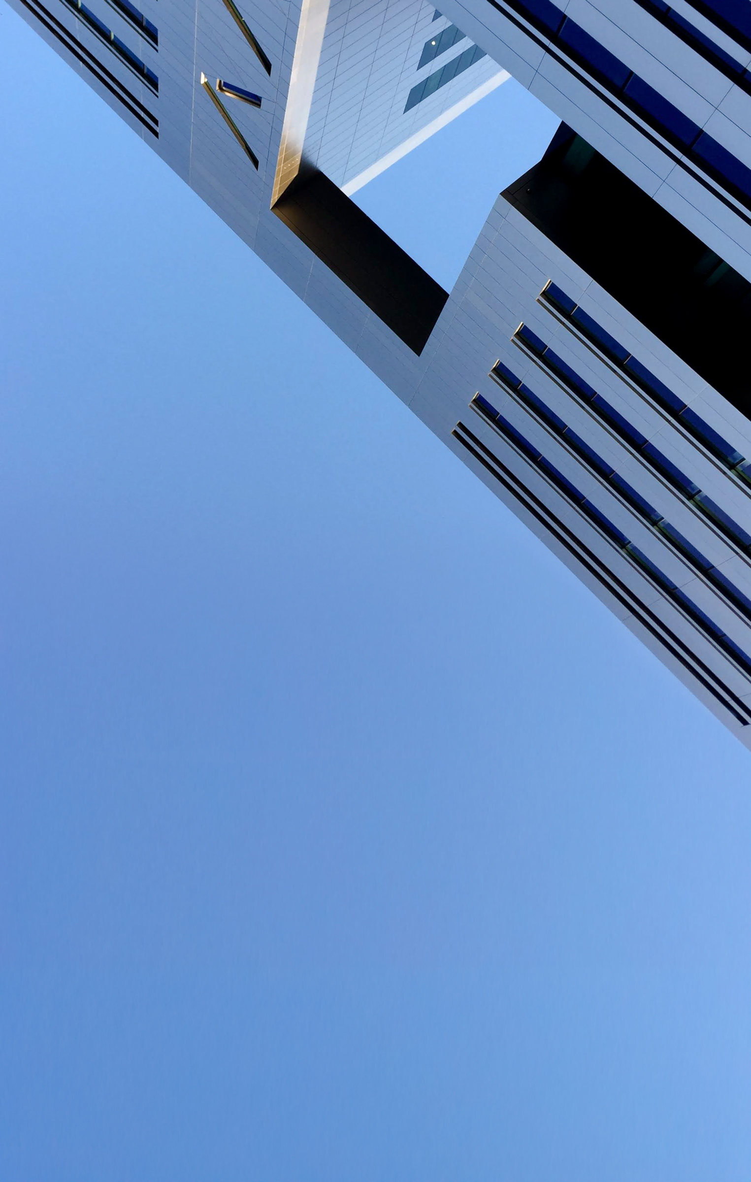 Modern high-rise building with a sky bridge connecting two towers against a clear blue sky.