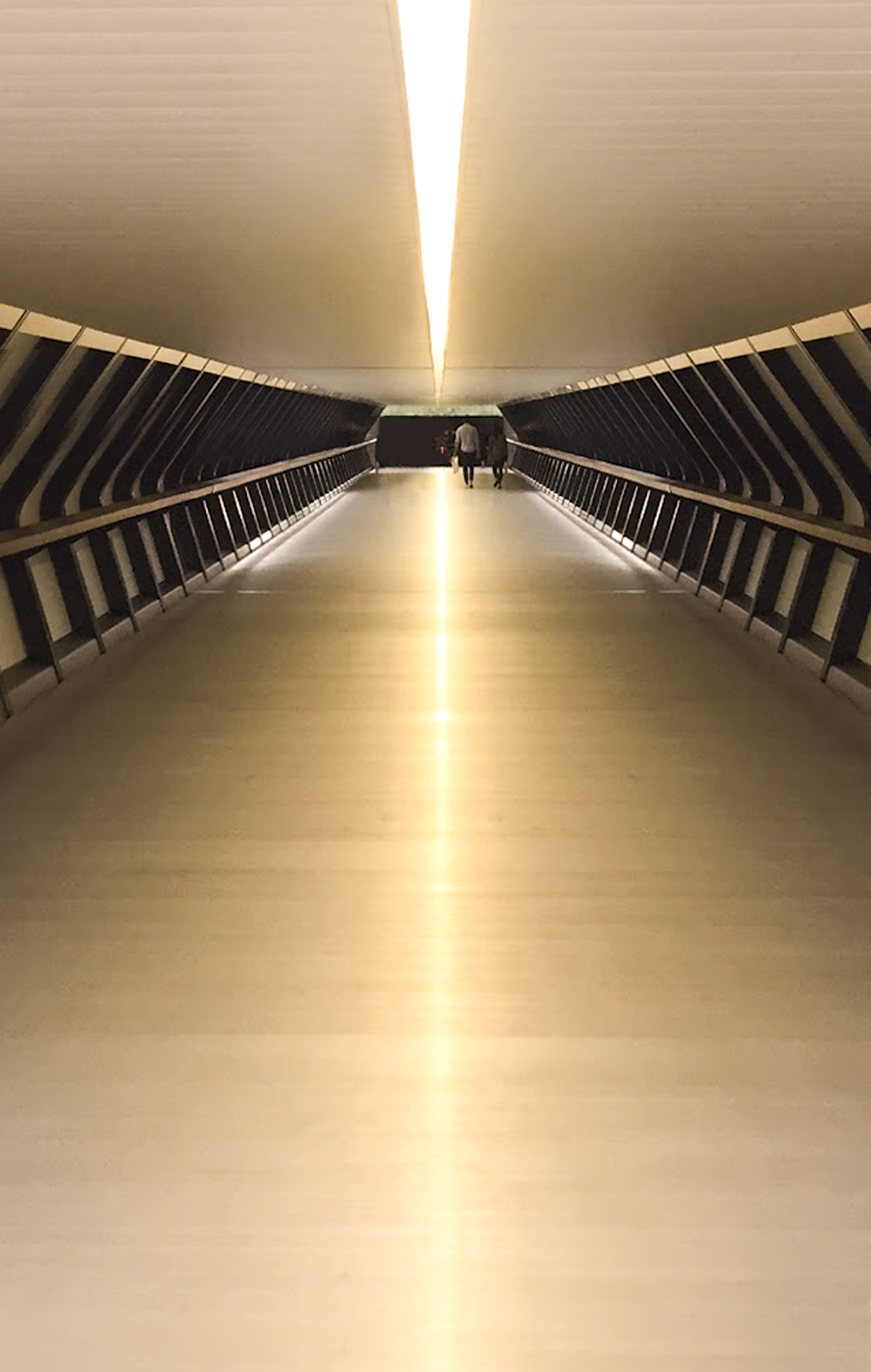 A couple walking hand in hand down a long, modern corridor with a glowing central light strip on the ceiling and floor.