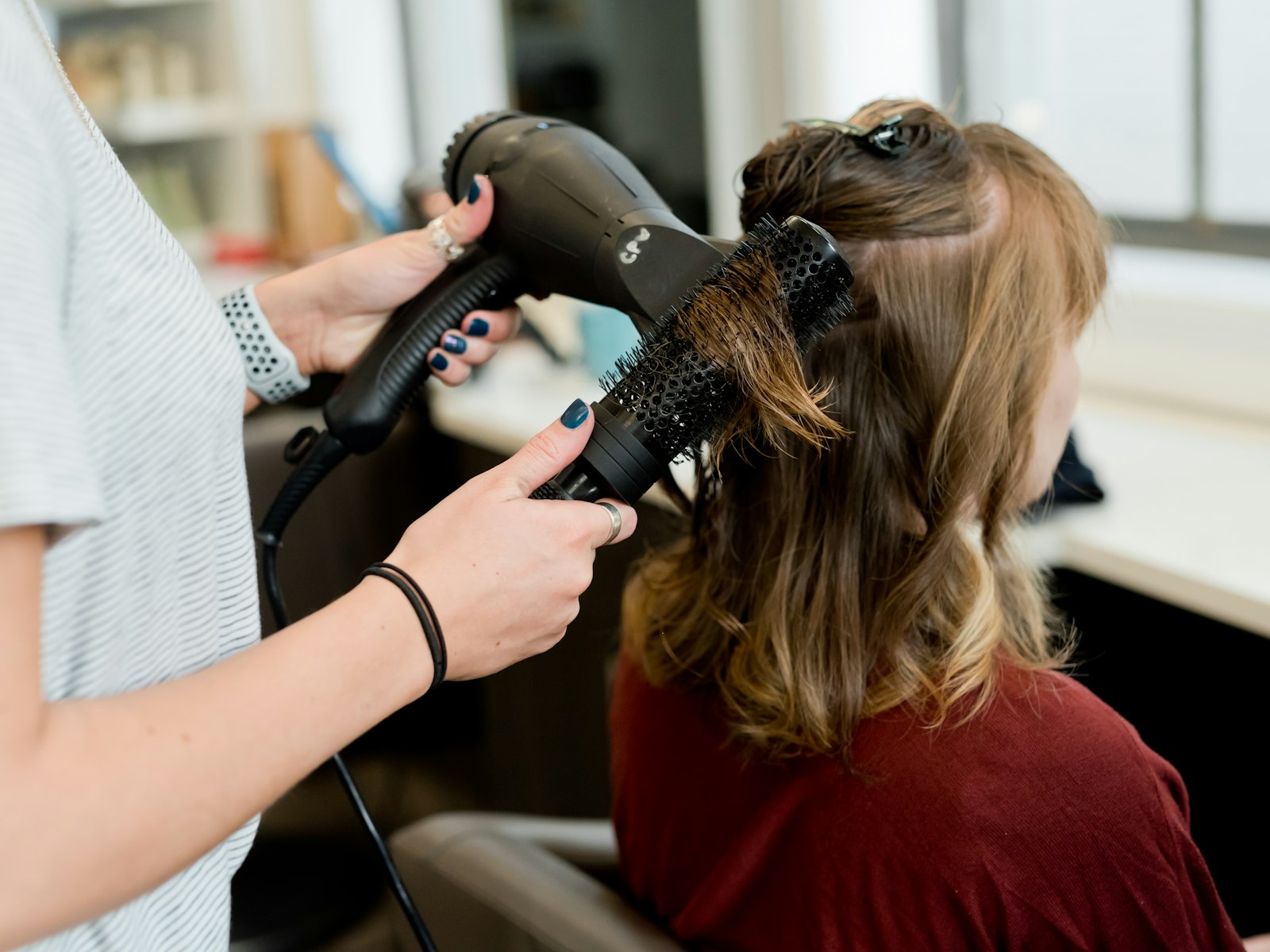 Hairstylist blow-drying a client's hair with a round brush