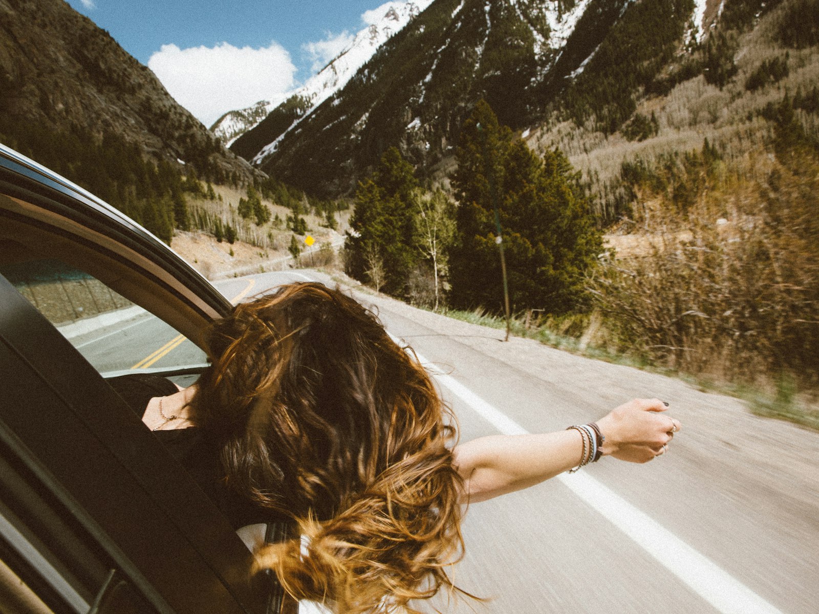 A passenger leaning out of a car window on an open road