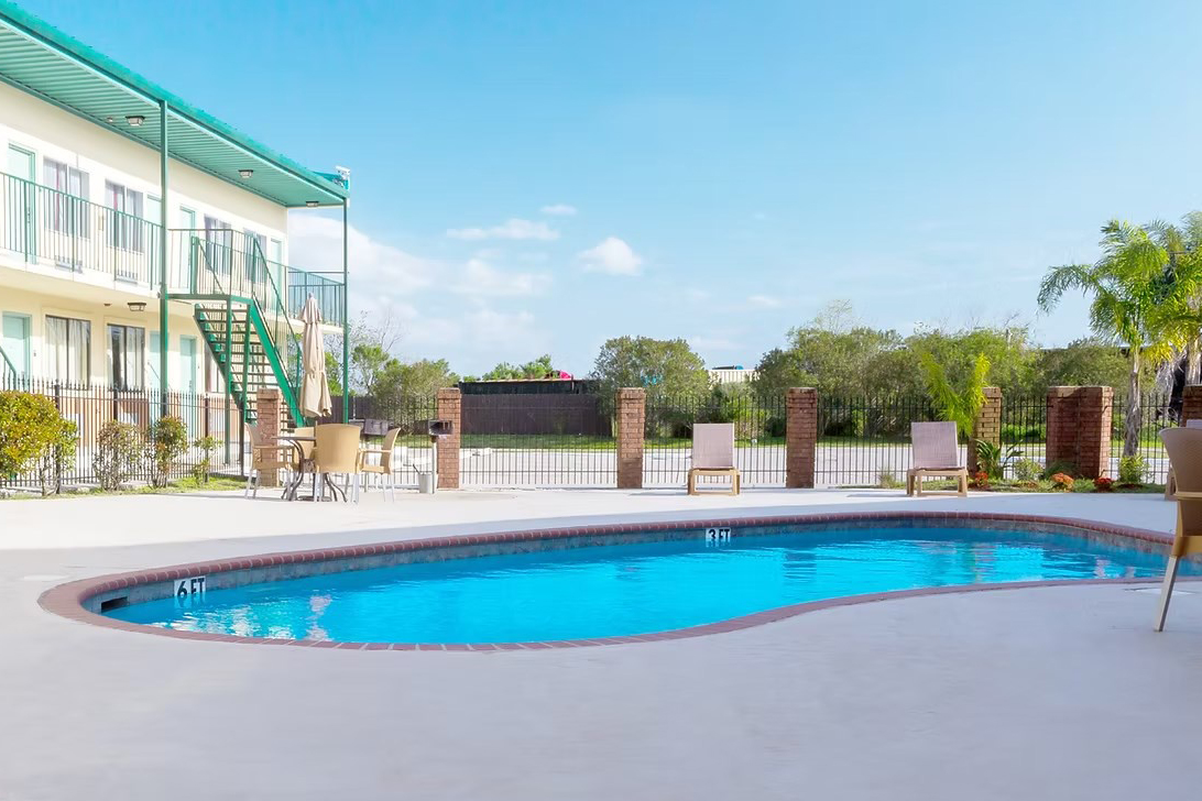 Outdoor swimming pool and jacuzzi next to a two-story building with green railings and stairs under a clear blue sky.