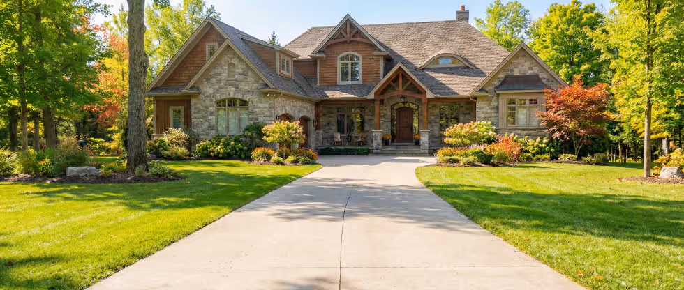Luxury stone house exterior with clean driveway and manicured lawn, showcasing spring property maintenance including gutter cleaning, pressure washing, and roof inspection services in Canada.