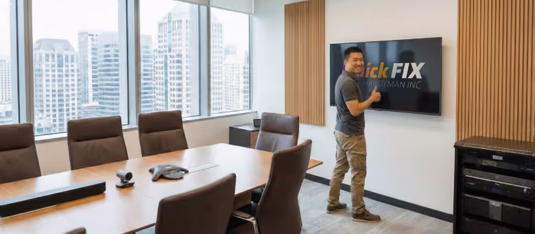 Professional boardroom TV and tech mounting service in Calgary, featuring a technician installing a large display on a conference room wall with precision alignment. | Quickfix Handyman Inc.