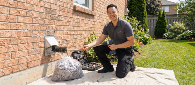 Professional dryer vent cleaning service in Calgary, featuring a technician using a specialized brush and vacuum system to remove lint buildup from an exterior wall vent | Quickfix Handyman Inc.