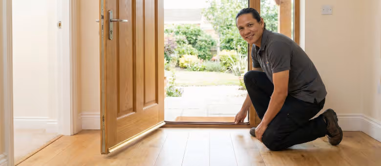 Professional door weatherstripping installation in Calgary, featuring a technician applying a high-quality seal to the base of a modern wooden entry door to improve home energy efficiency | Quickfix Handyman Inc.