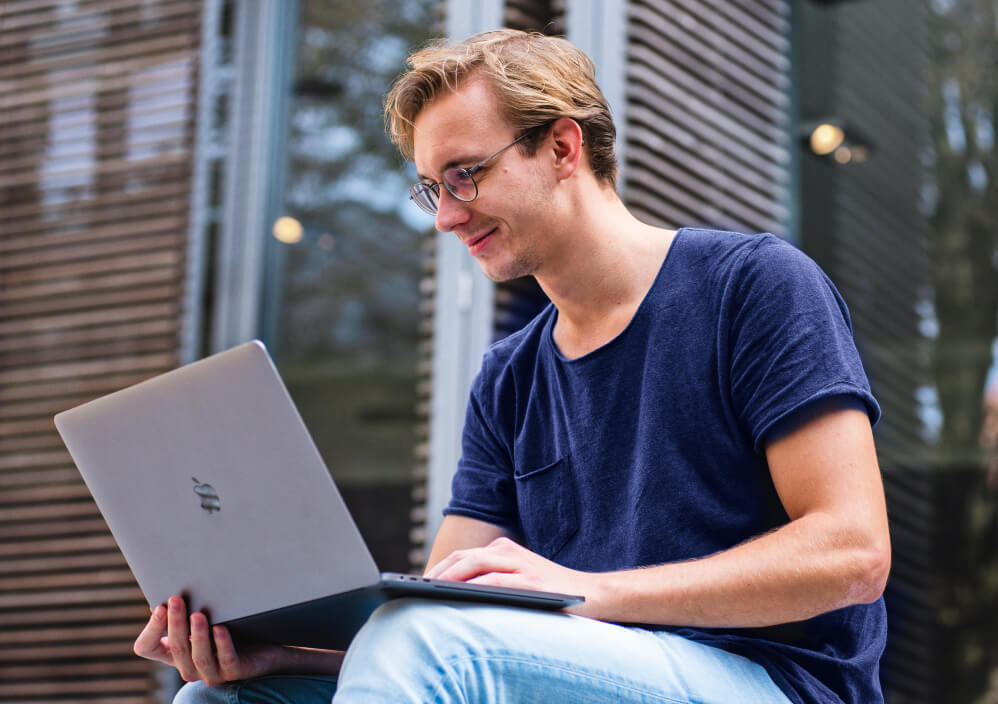 Mann bruker laptop utendørs, fokusert på skjermen.