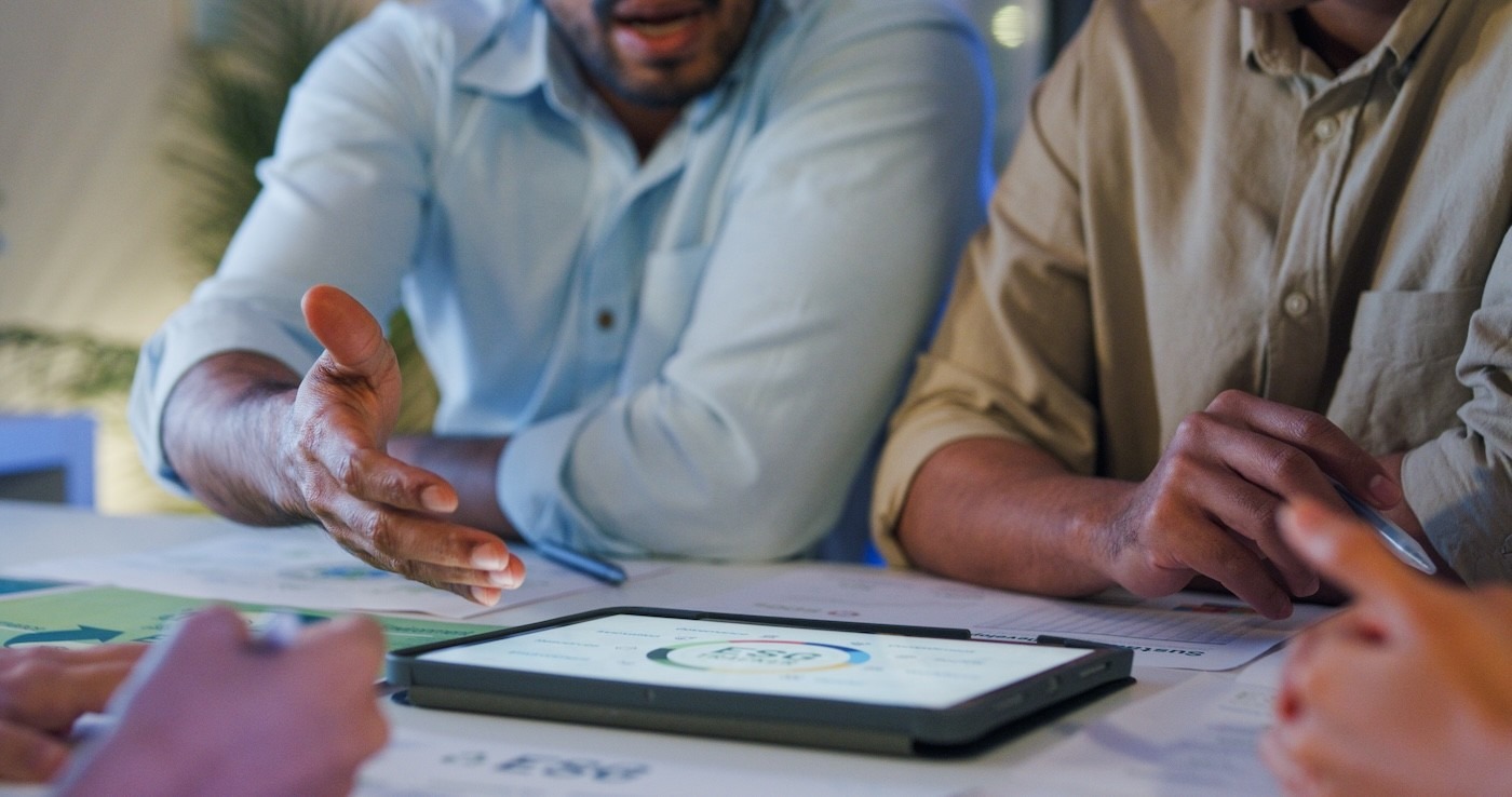 Mitarbeiter in einer Besprechung diskutieren über Zahlen auf einem Tablett