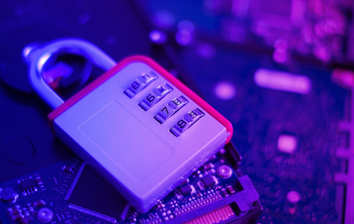 Ein silbernes Zahlenschloss liegt auf einer internen Festplatte und einer Leiterplatte, beleuchtet in kühlem Blau und Violett.