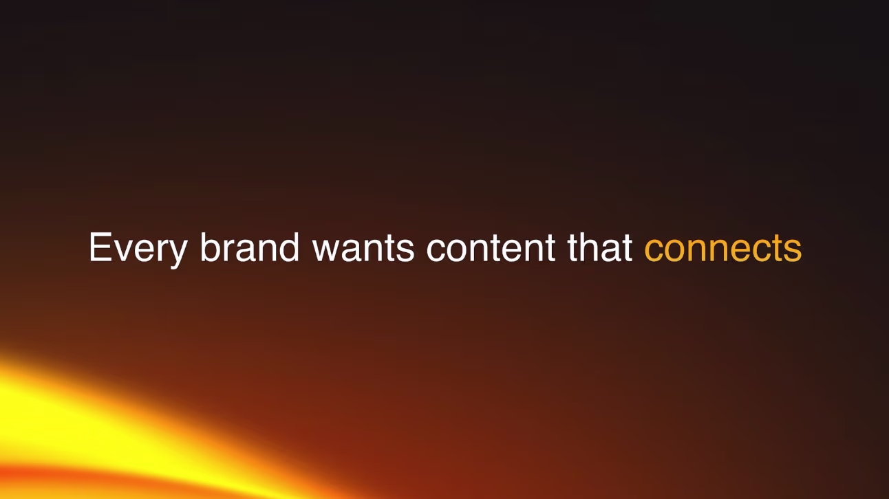 A man with gray hair and glasses is smiling, wearing a suit and tie, sitting in a brightly lit room with framed art and photos on the wall behind him.