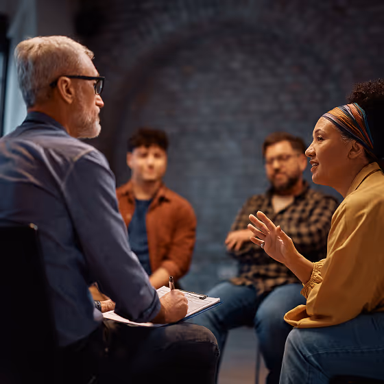 A woman speaks animatedly while three people listen attentively in a group discussion setting.