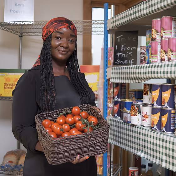 Smiling woman wearing a red headscarf holding a basket of fresh cherry tomatoes in a grocery store aisle.