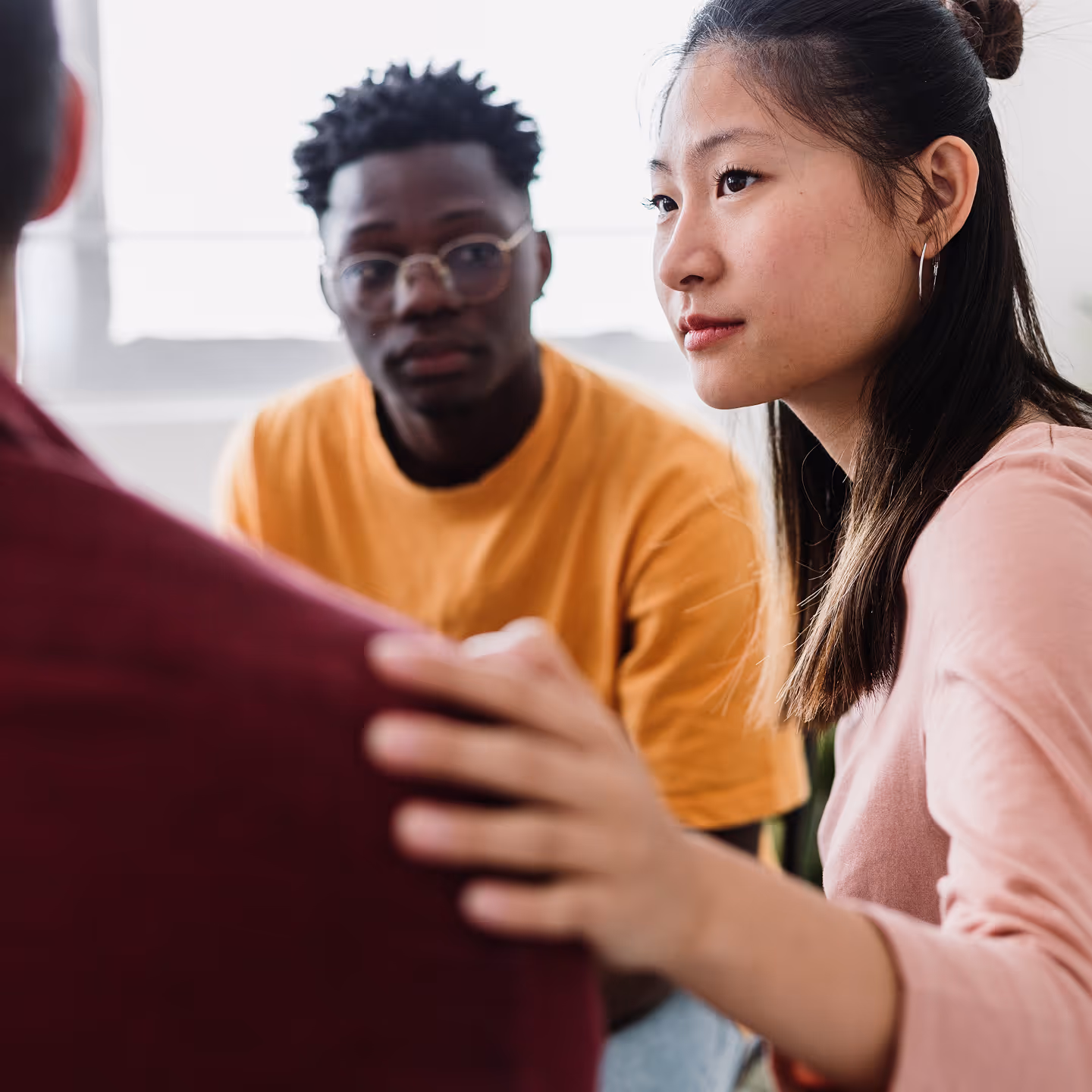 Young woman with hand on a person's shoulder comforting them while a young man looks on attentively.