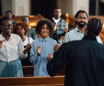 A diverse group of people standing and clapping inside a church during a service.