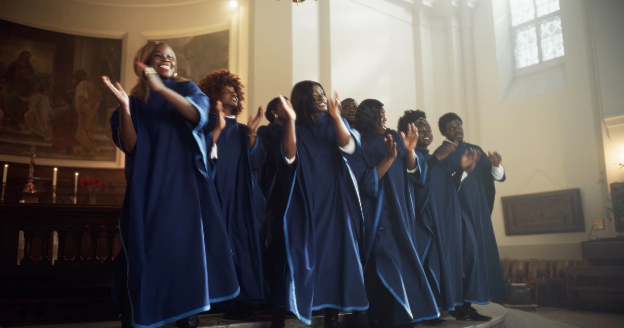 Group of people in blue choir robes singing and clapping inside a church.