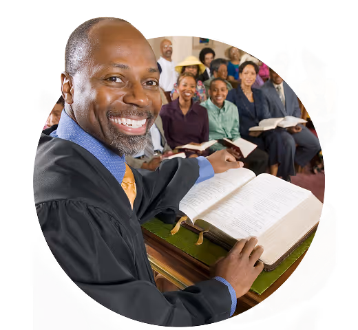 Smiling male preacher in black robe holding an open Bible with a diverse congregation behind him.