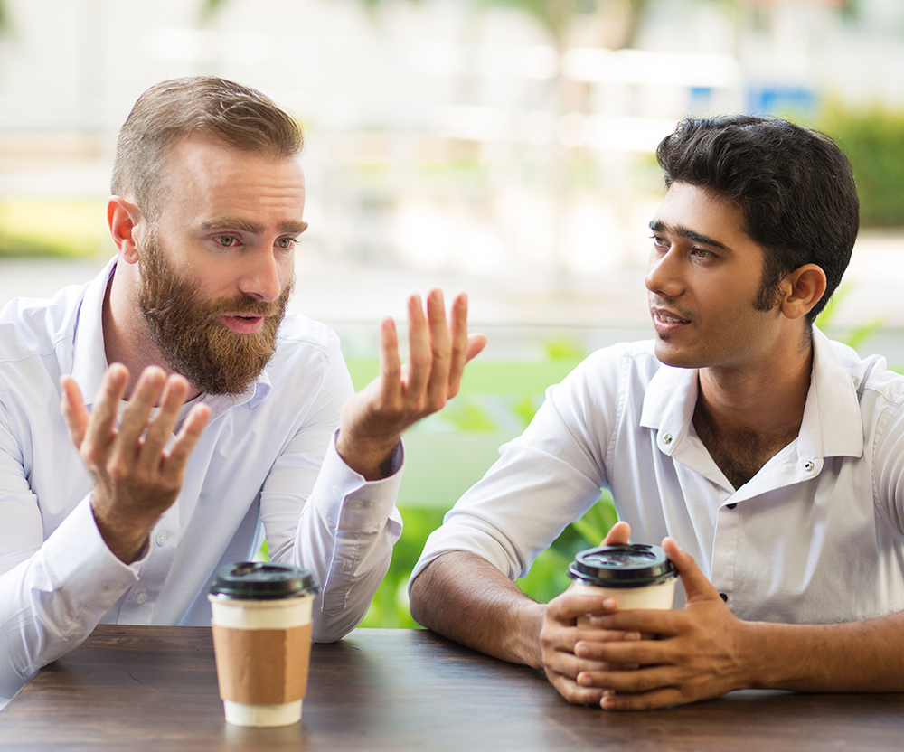 Young man showing a tablet to an elderly woman with a cane, sitting together indoors near a window.