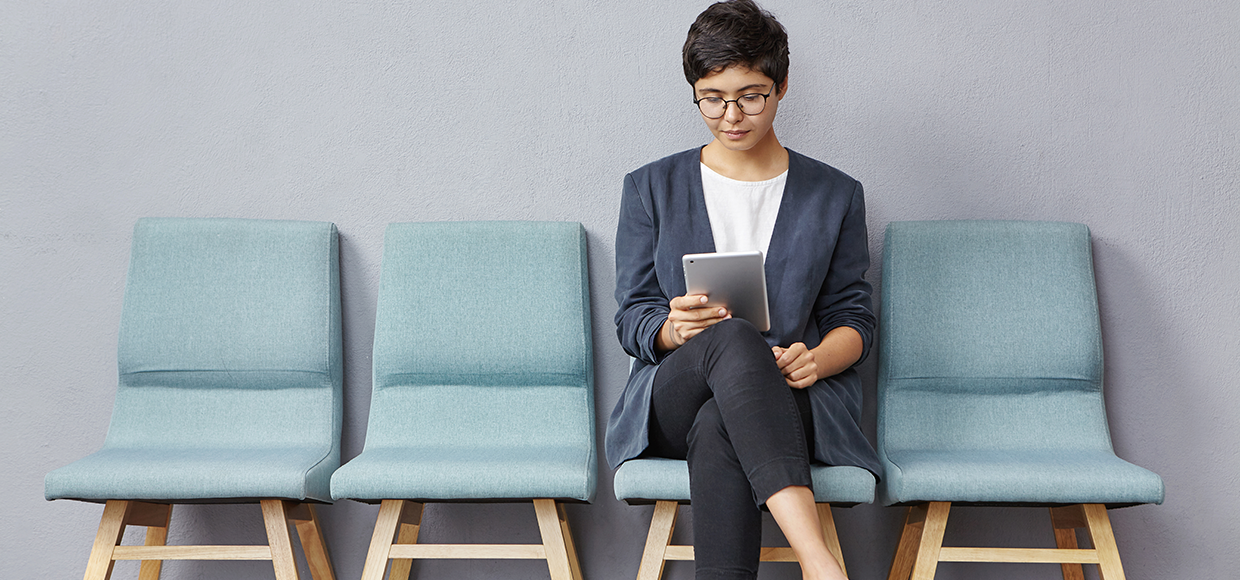 Man sitting in a chair reading a book to a baby on his lap with a dog sitting nearby in a cozy room.