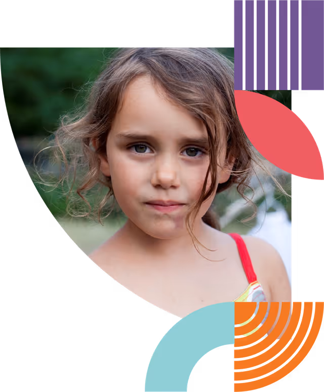 A young girl with brown curly hair and blue eyes looking directly at the camera, wearing a red strap top with a green blurred background.