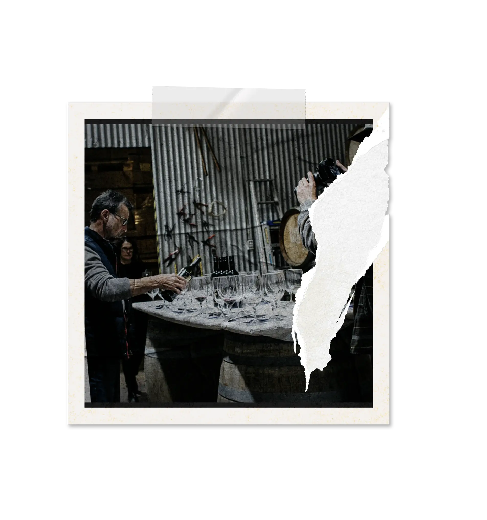 Man pouring wine into glasses arranged on a table covered with a gray cloth in a rustic cellar setting.