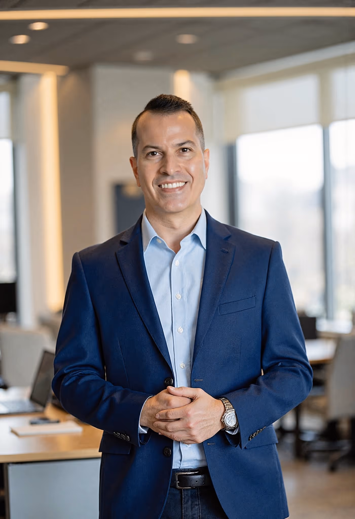 Nick (Magic Number Founder) smiling in a blue blazer and light blue shirt standing in a modern office setting with hands clasped.