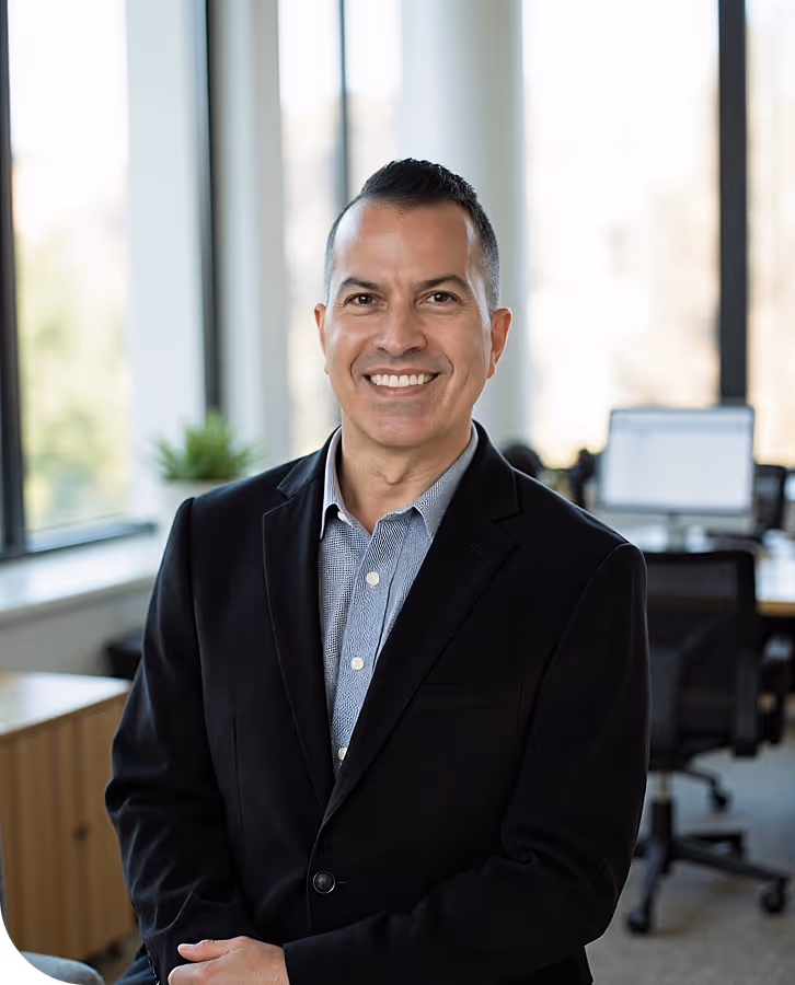Nick, Magic Number founder, smiling in a black blazer and checkered shirt in a modern office with windows and desks.