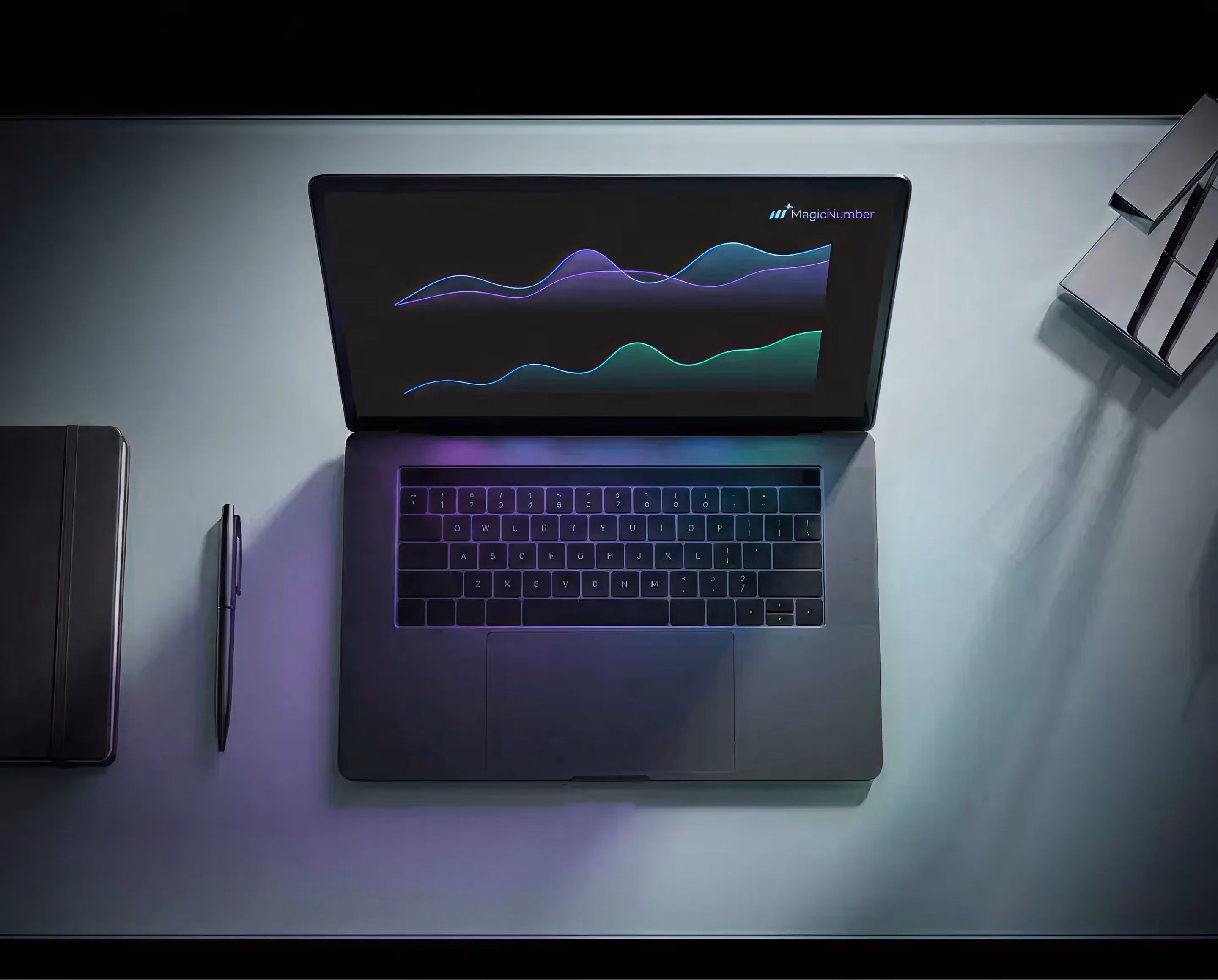 Open laptop on a desk displaying colorful wave graphs with the text 'MagicNumber' on the screen, next to a closed notebook and a pen.