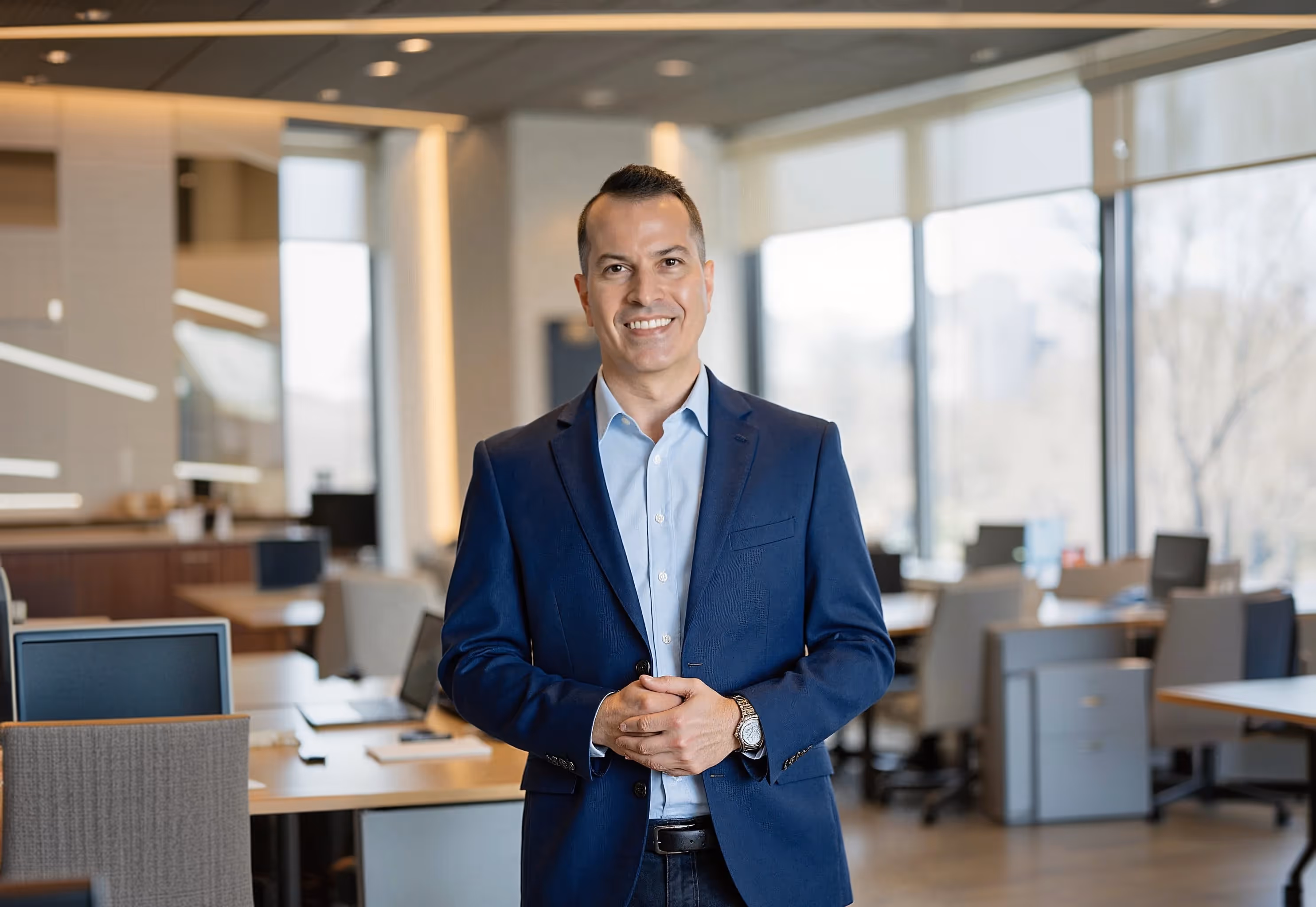 Nick, Magic Number founder, smiling in a blue blazer and light blue shirt standing in a modern office space with desks and large windows.
