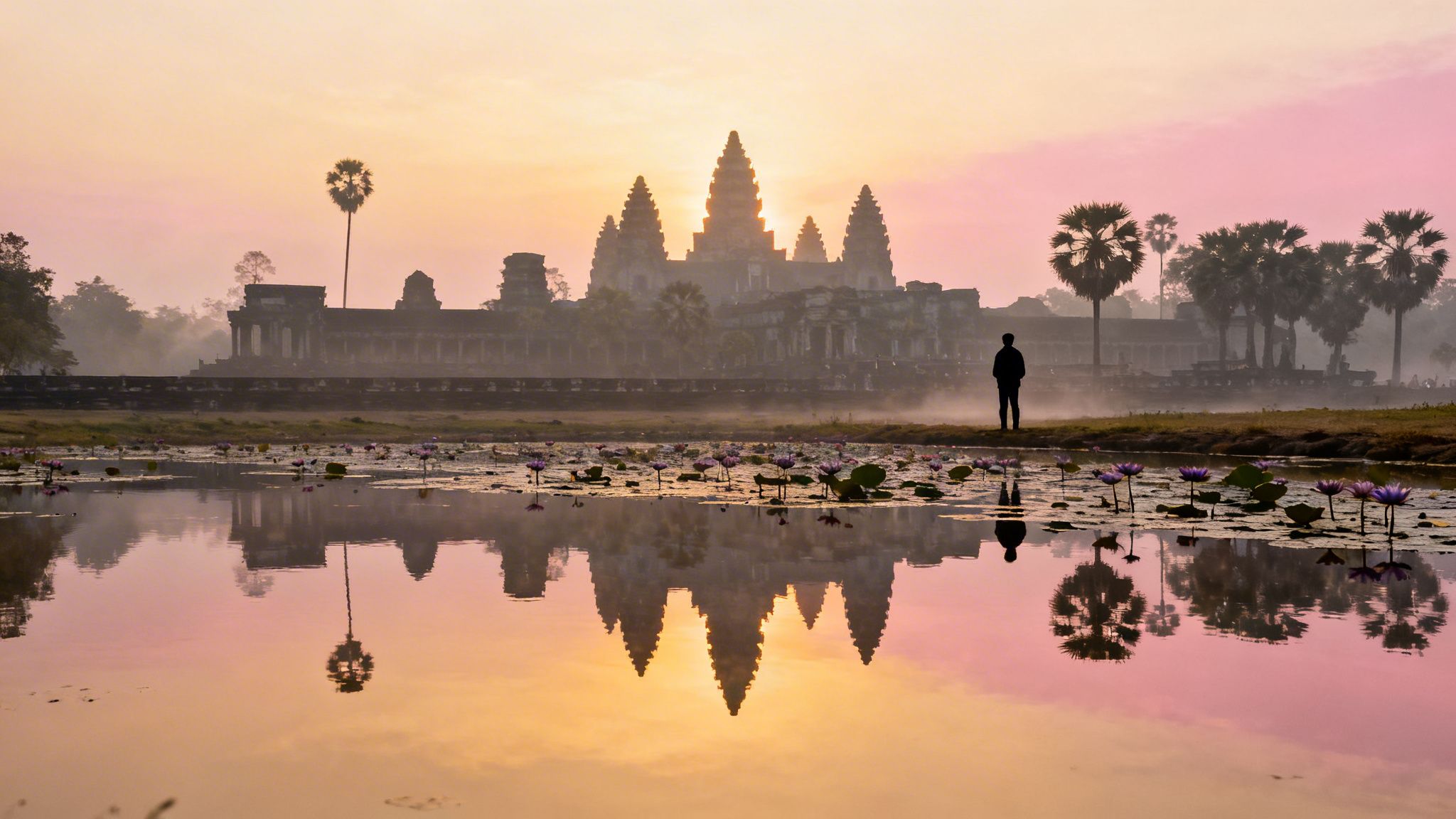 Sunrise at Angkor Wat, Cambodia, with its reflection in a lily pond and a lone observer.