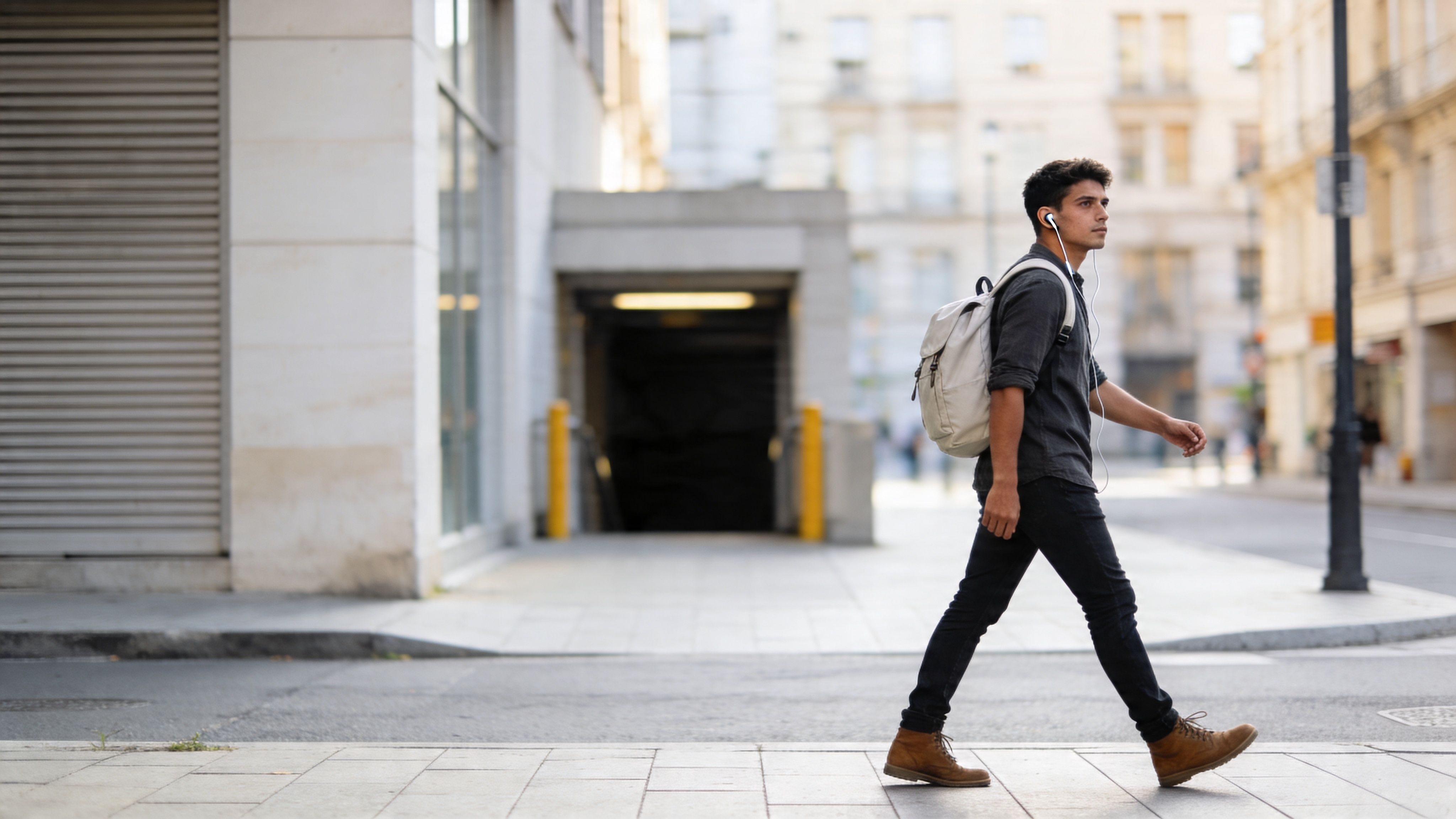 A young man with a backpack and headphones walking down a city street while traveling solo.