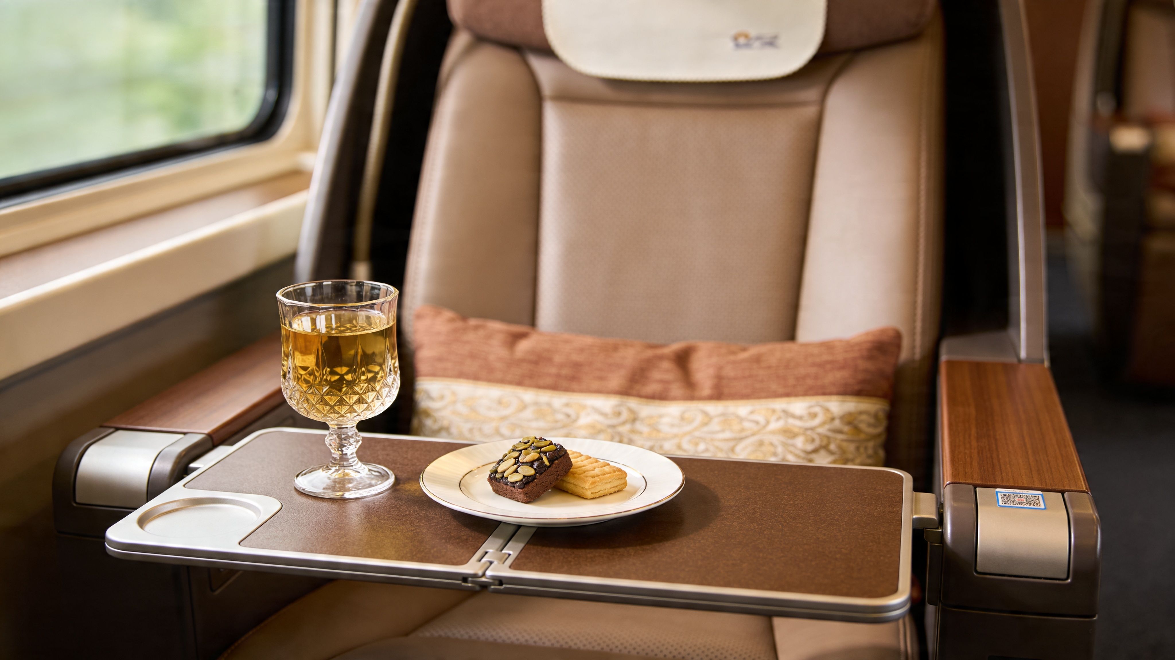 A luxurious train seat featuring a wooden tray table with a glass of juice and snacks.