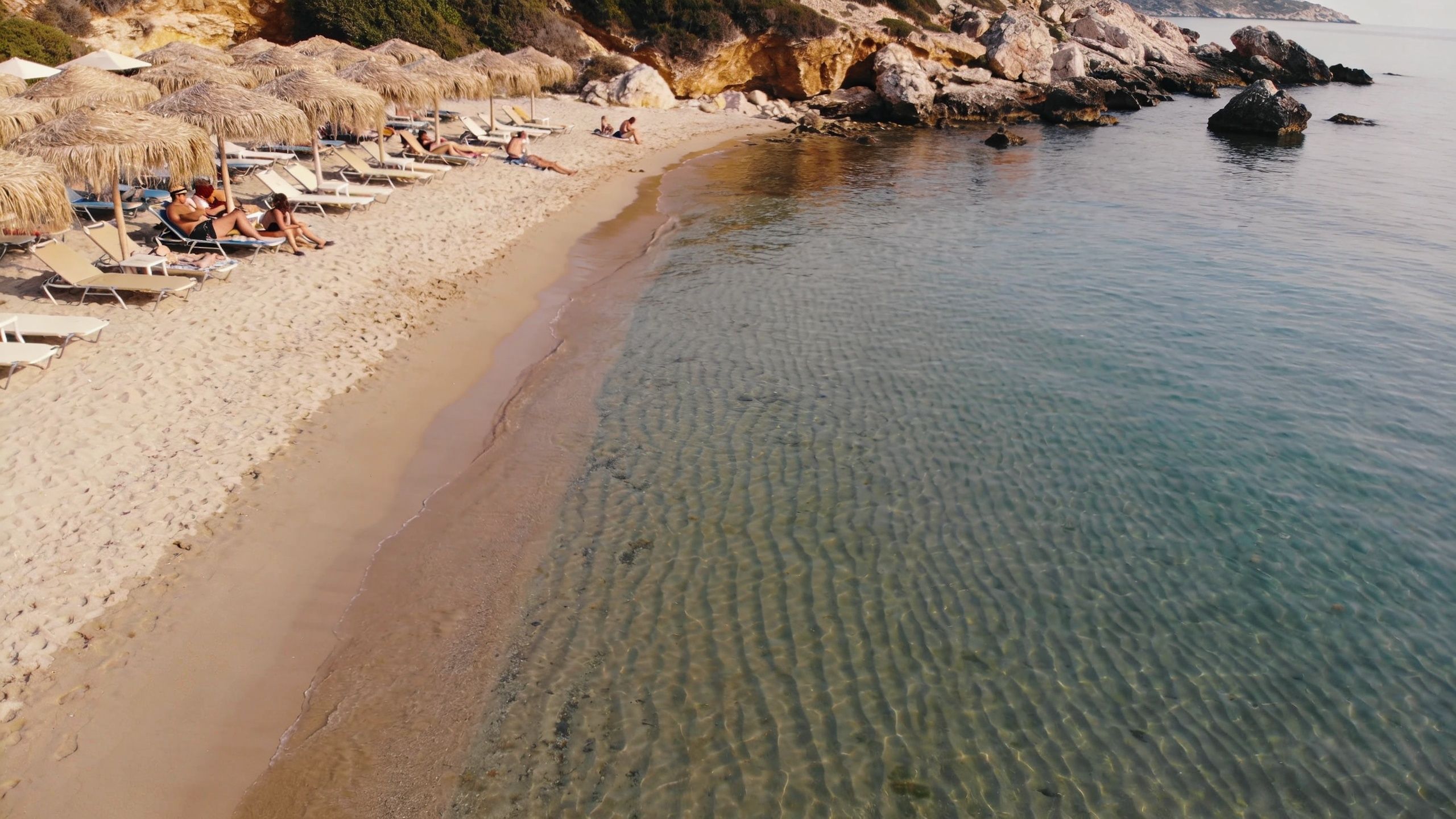 A scenic view of Agios Ioannis beach with umbrellas and lounge chairs on sandy shore by clear water.