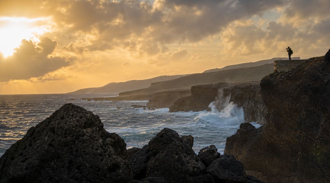 A photographer stands on a cliffside looking at the ocean during a golden hour sunset in Barbados.