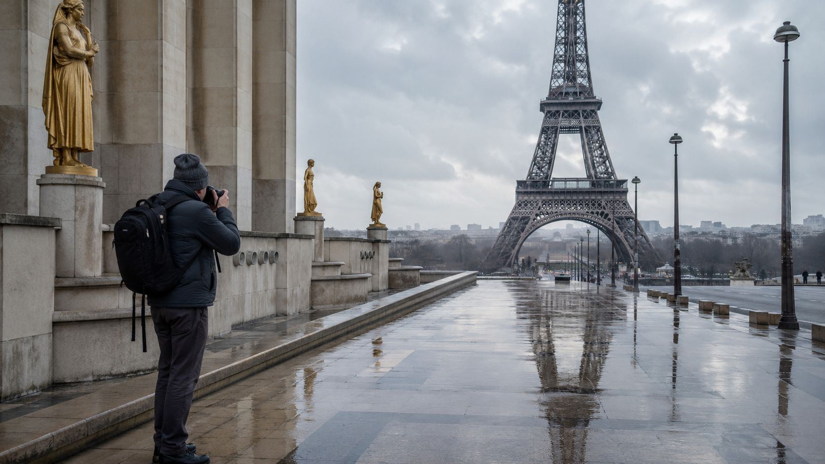 A photographer with a backpack taking pictures of the Eiffel Tower from Trocadero on a rainy day.