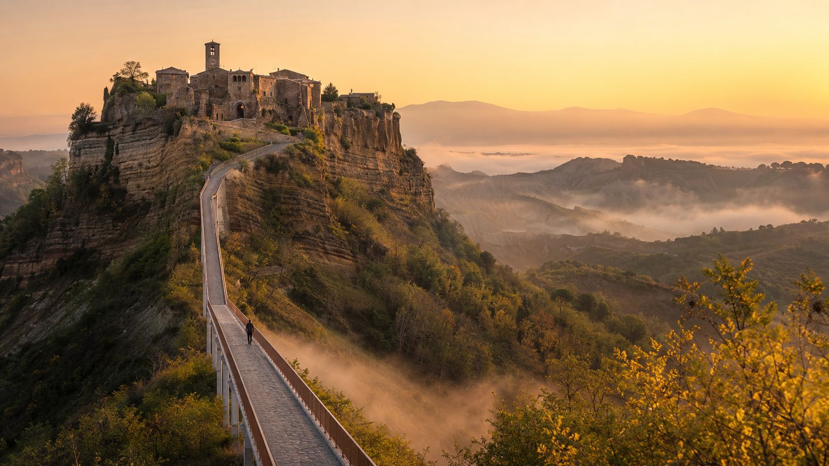 A lone person walks across a pedestrian bridge leading to the historic hilltop village of Civita di Bagnoregio.