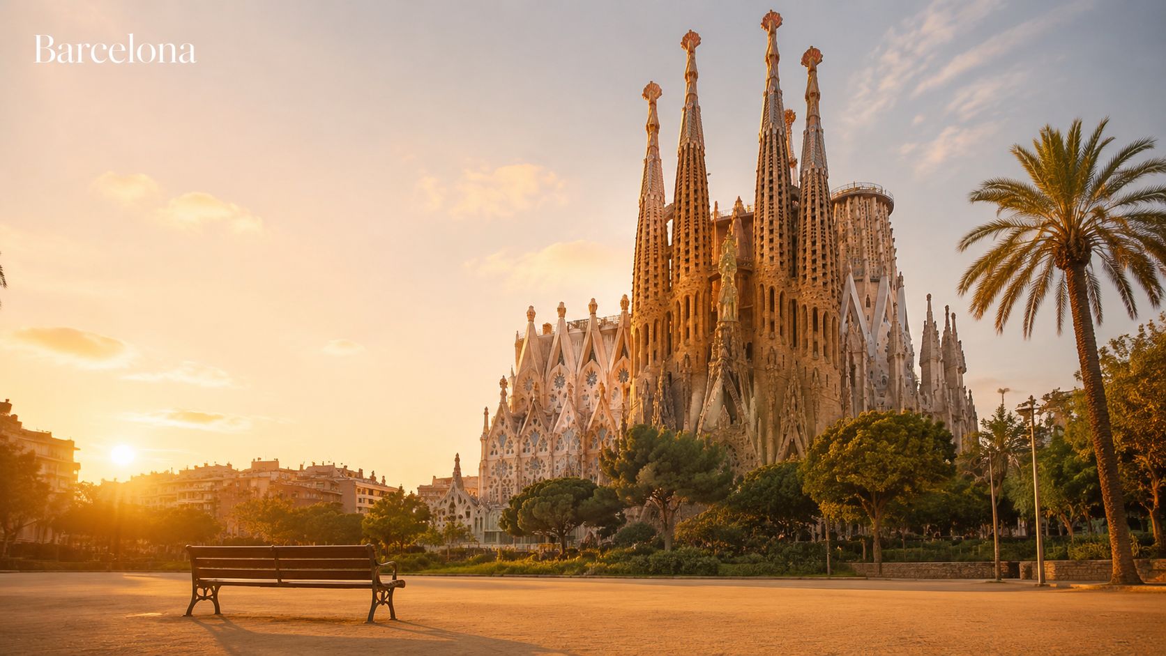 A scenic sunset view of the Sagrada Familia basilica in Barcelona with a park bench nearby.