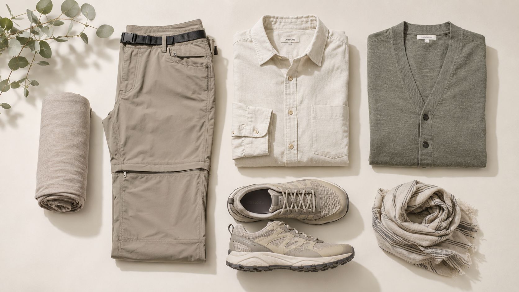 A flat lay of travel clothing, including pants, a button-down shirt, a cardigan, shoes, and accessories.